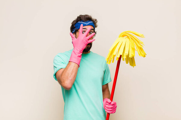 молодой человек выглядит шокированным, испуганным или испуганным, закрывая лицо рукой и подглядывая между пальцами