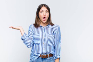 Güzel bir kadın şaşırmış ve şoka uğramış görünüyor, çenesi düşmüş, elinde açık bir elle bir nesne tutuyor.
