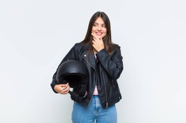 Güzel bir kadın mutlu, kendinden emin bir ifadeyle gülümsüyor, çenesinde elleri, merak ediyor ve yan tarafa bakıyor.