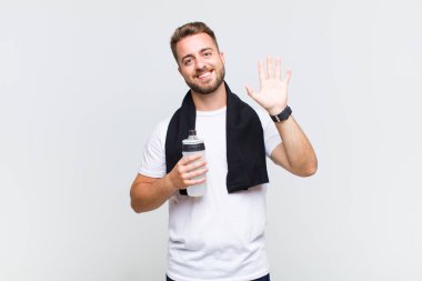 Genç adam mutlu ve neşeyle gülümsüyor, el sallıyor, seni selamlıyor ve selamlıyor, ya da hoşça kal diyor.