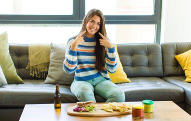 Güzel bir kadın, kendine güvenerek gülümseyerek kendi geniş gülümsemesini, pozitif, rahat, tatmin olmuş tavrını gösterir.