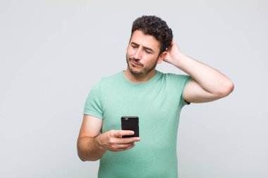 Genç adam şaşkın ve şaşkın hissediyor, başını kaşıyor ve yana bakıyor.