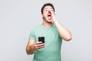 Genç adam mutlu, heyecanlı ve pozitif hissediyor. Elleri ağızda, bağırıyor.