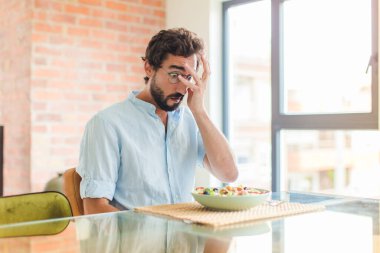 Sakallı adam şok olmuş, korkmuş ya da korkmuş görünüyor. Yüzü elle kaplanmış ve parmaklarının arasından gizlice bakıyor.