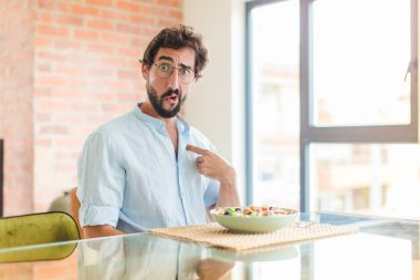Sakallı adam şok olmuş ve ağzı açık, kendini işaret ederek şaşırmış görünüyor.
