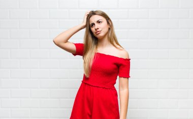 Sarışın kadın şaşkın ve şaşkın hissediyor, kafasını kaşıyor ve yan tarafa bakıyor.