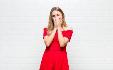 Sarışın kadın mutlu, neşeli, şanslı ve şaşkın görünüyor. İki eliyle ağzını kapatıyor.