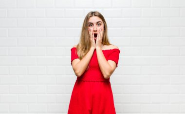 Sarışın kadın şok olmuş ve korkmuş hissediyor, ağzı açık ve elleri yanaklarında korkmuş görünüyor.