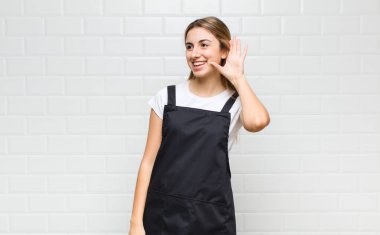 Sarışın kadın gülümsüyor, tuhaf bir şekilde yan tarafa bakıyor, dedikoduları dinlemeye ya da bir sırrı duymaya çalışıyor.