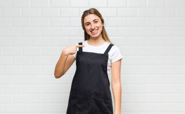 Sarışın kadın gururlu, kendinden emin ve mutlu görünüyor, gülümsüyor ve kendini işaret ediyor ya da bir numara işareti yapıyor.