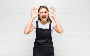 Sarışın kadın panik ya da öfke içinde bağırıyor, şok olmuş, korkmuş ya da öfkeli, elleri başının yanında.