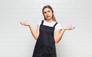 blonde woman shrugging with a dumb, crazy, confused, puzzled expression, feeling annoyed and clueless