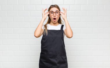 Şok olmuş, şaşırmış ve şaşırmış hisseden sarışın bir kadın, elinde şaşkın, inançsız bir bakışla gözlük tutuyor.