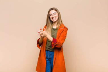 Sarışın kadın kendini mutlu ve başarılı hissediyor. Gülümsüyor ve alkışlıyor. Alkışlarla tebrik ediyor.