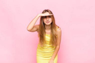 Sarışın kadın şaşkınlık ve şaşkınlık içinde bakıyor. Alnı açık, uzaklara bakıyor, izliyor ya da arıyor.