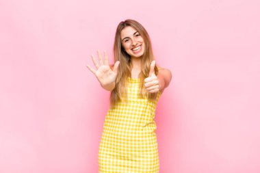 Sarışın kadın gülümsüyor ve arkadaş canlısı görünüyor, altı ya da altıncı numarayı gösteriyor, eli önde, geri sayıyor.