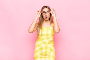 Şok olmuş, şaşırmış ve şaşırmış hisseden sarışın bir kadın, elinde şaşkın, inançsız bir bakışla gözlük tutuyor.