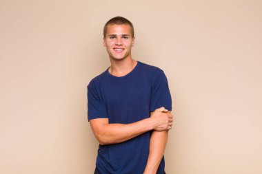 Sarışın adam utangaç ve neşeli bir şekilde gülüyor, arkadaş canlısı ve olumlu ama güvensiz bir tavırla.