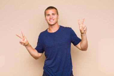 Sarışın adam gülümsüyor ve mutlu görünüyor, arkadaş canlısı ve tatmin olmuş, zafer ya da barış işareti yapıyor.