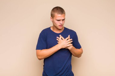 Sarışın adam üzgün, yaralı ve kalbi kırık görünüyor, iki elini de kalbe yakın tutuyor, ağlıyor ve bunalımda.