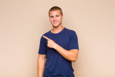 Sarışın adam neşeyle gülümsüyor, mutlu hissediyor ve kenarı ve yukarıyı işaret ediyor, fotokopi uzayındaki nesneleri gösteriyor.