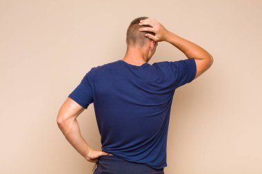 Sarışın adam düşünüyor ya da şüphe ediyor, kafasını kaşıyor, kafası karışık ve kafası karışık hissediyor, arkaya ya da arkaya bakıyor.