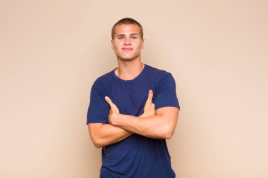 Sarışın adam kollarını kavuşturup mutlu bir şekilde gülüyor, rahat, pozitif ve tatmin edici bir pozla.