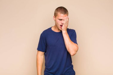 Sarışın bir adam uykulu, sıkılmış ve esniyor, baş ağrısı ve yüzünün yarısını kaplayan bir elle.