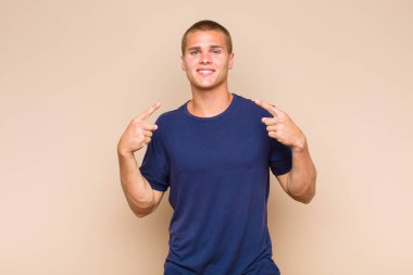 Sarışın adam kendinden emin bir şekilde gülümseyerek kendi geniş gülüşünü, pozitif, rahat, tatmin olmuş tavrını gösteriyor.