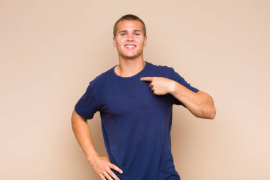 Sarışın adam mutlu, gururlu ve şaşırmış görünüyor, neşeli bir şekilde kendini gösteriyor, kendinden emin ve kibirli hissediyor.