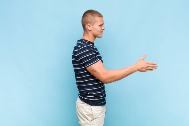 Sarışın adam gülümsüyor, seni selamlıyor ve başarılı bir anlaşma için el sıkışmayı teklif ediyor.