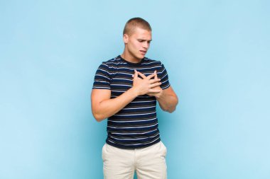 Sarışın adam üzgün, yaralı ve kalbi kırık görünüyor, iki elini de kalbe yakın tutuyor, ağlıyor ve bunalımda.