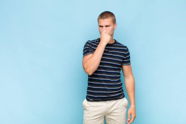 Sarışın adam iğreniyor, kötü ve nahoş bir koku duymamak için burnunu tutuyor.