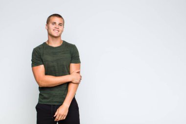 Sarışın adam utangaç ve neşeli bir şekilde gülüyor, arkadaş canlısı ve olumlu ama güvensiz bir tavırla.