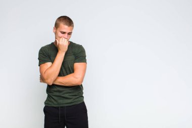 Sarışın adam ciddi, düşünceli ve endişeli, eli çenesine değmiş, yan yan bakıyor.