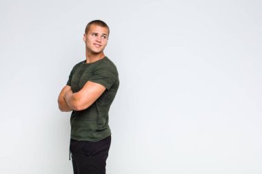 Sarışın adam neşeyle gülümsüyor, mutlu, tatmin olmuş ve rahatlamış hissediyor, kollarını kavuşturup yan tarafa bakıyor.