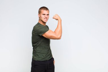 Sarışın adam kendini mutlu, tatmin olmuş ve güçlü hissediyor, kaslı ve formda, spor salonundan sonra güçlü görünüyor.