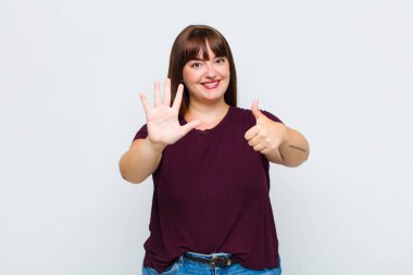 Kilolu bir kadın gülümsüyor ve arkadaş canlısı görünüyor. Elleri önde, geriye doğru sayarak altı ya da altıncı numarayı gösteriyor.