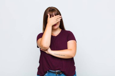 Aşırı kilolu bir kadın stresli, utanmış ya da üzgün görünüyor, baş ağrısı var, yüzünü eliyle kapatıyor.