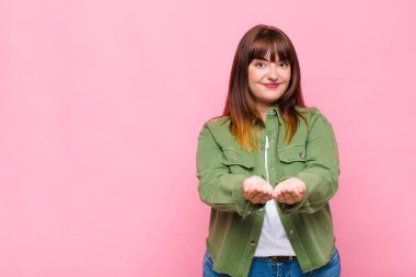 şişman kadın mutlu bir şekilde gülümsüyor, arkadaş canlısı, kendinden emin, pozitif bakışlı, bir nesne ya da konsept sunuyor ve gösteriyor.