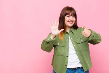 Kilolu bir kadın gülümsüyor ve arkadaş canlısı görünüyor. Elleri önde, geriye doğru sayarak altı ya da altıncı numarayı gösteriyor.