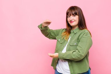 İki eli de kenarda olan bir objeyi tutan kilolu bir kadın fotokopi alanında bir nesneyi gösteriyor, sunuyor ya da reklamını yapıyor.