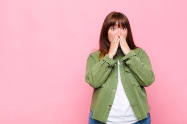 Kilolu bir kadın endişeli, üzgün ve korkmuş hissediyor. Ağzını ellerle kapatıyor. Endişeli görünüyor ve mahvolmuş görünüyor.