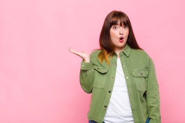 Şişman kadın şaşırmış ve şok olmuş görünüyor, çenesi düşmüş ve eli açık bir objeyi tutuyor.