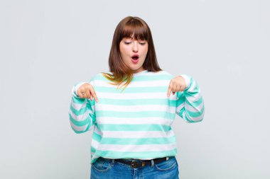 İki eliyle aşağıya bakan ağzı açık şişman bir kadın. Şok olmuş, şaşırmış ve şaşırmış görünüyor.