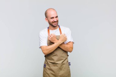 Kel adam neşeyle gülümsüyor ve kutluyor, yumruklarını sıkıp kollarını kavuşturuyor, mutlu ve pozitif hissediyor.