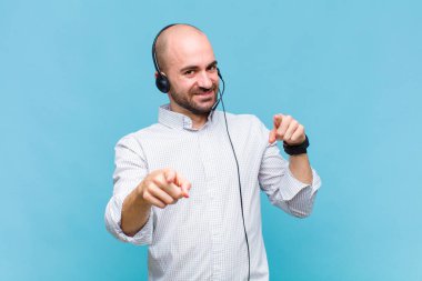 Kel adam mutlu ve kendinden emin hissediyor, kamerayı iki eliyle gösteriyor ve gülüyor, seni seçiyor.