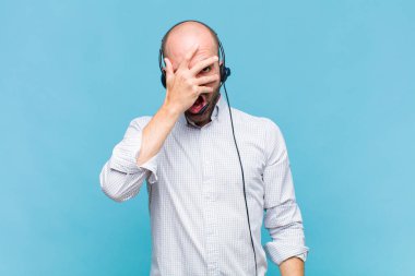 Kel adam şok olmuş, korkmuş ya da korkmuş görünüyor. Yüzü elle örtülmüş ve parmaklarının arasından gizlice bakıyor.