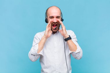 Kel adam mutlu, heyecanlı ve pozitif hissediyor. Elleri ağızda, bağırarak bağırıyor.