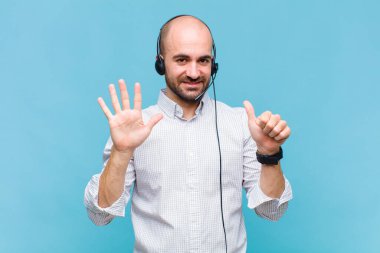 Kel adam gülümsüyor ve arkadaş canlısı görünüyor, altı ya da altıncı numarayı gösteriyor, eli önde, geriye doğru sayıyor.